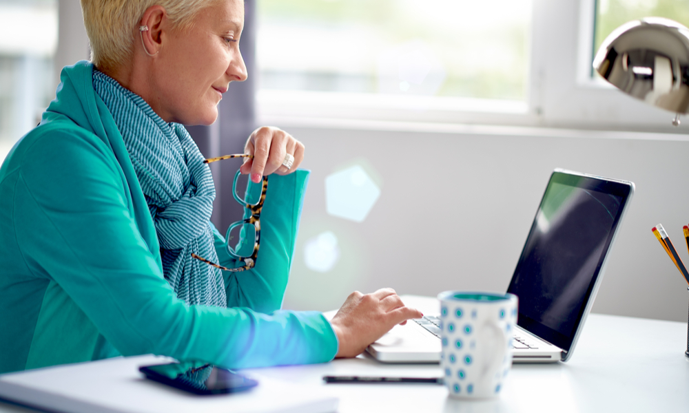 Senior sitting at the desk in modern office and using laptop