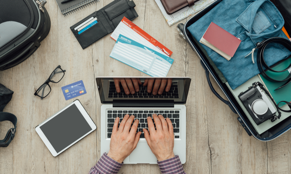 Traveler getting ready for a trip, he is packing his bag and planning a journey online using a laptop