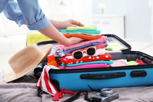 Female hands packing traveler case on bed, closeup