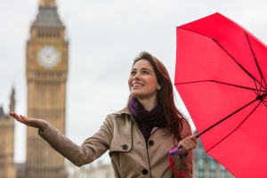 young woman with a red umbrella, hand out, checking for rain by Big Ben, London, England