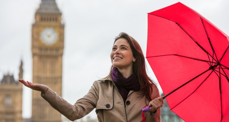 young woman with a red umbrella, hand out, checking for rain by Big Ben, London, England