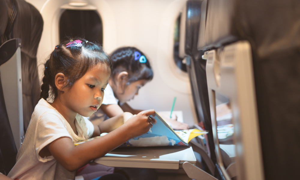 girls traveling by an airplane and spending time by drawing and reading a book during the flight