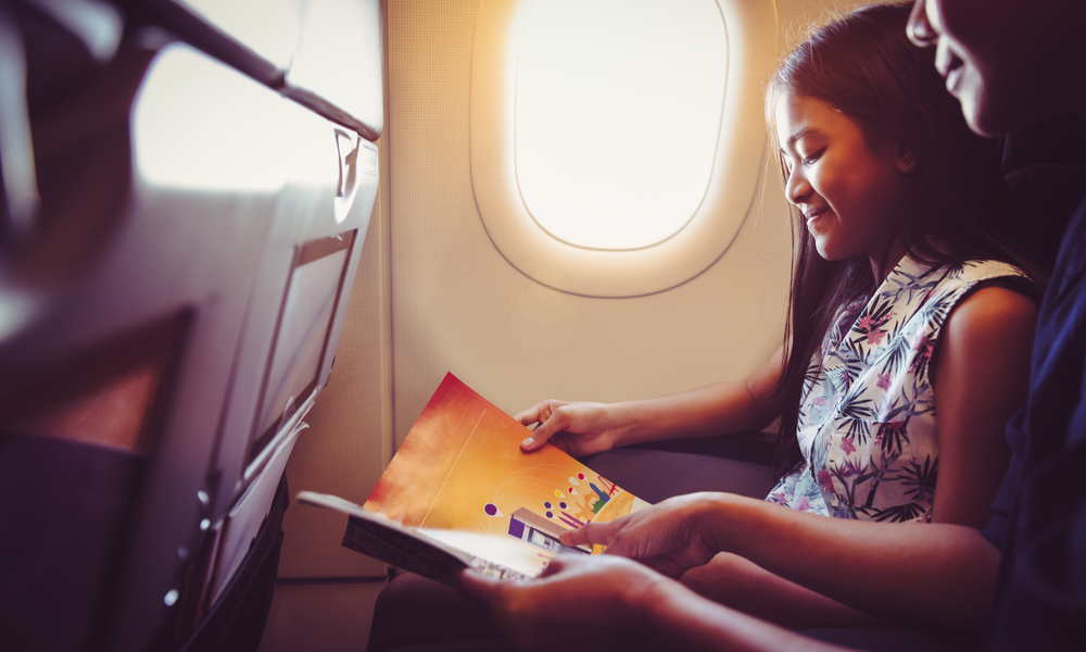 Mother with daughter sit on their place in airplane economy class and read a magazine