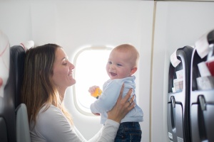 Young mom, playing and breastfeeding her toddler boy on board of aircraft,