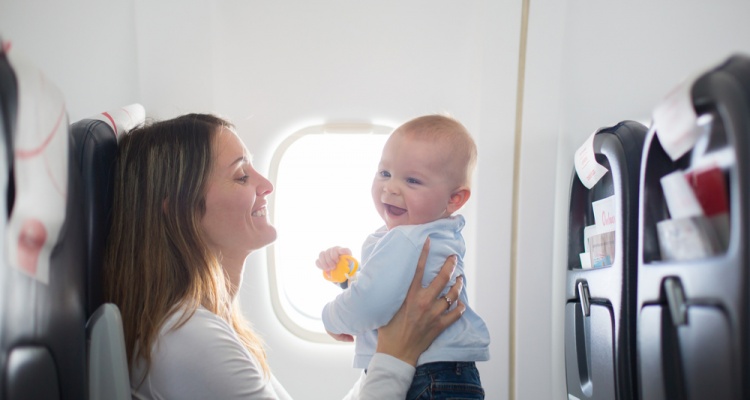 Young mom, playing and breastfeeding her toddler boy on board of aircraft,