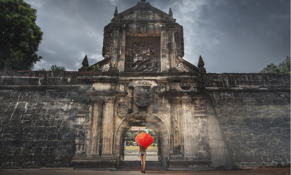 Woman with red umbrella stay at entrance gate in Fort Santiago, Intramuros city in Manila, Philippines