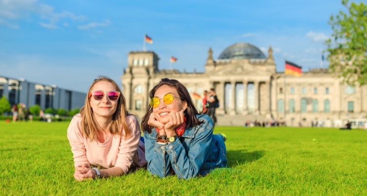 Two Young happy girls wearing sun glasses lying on a grass and have fun in front of the Bundestag building in Berlin