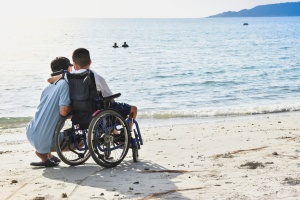 boy in a wheelchair on the beach with his arm around a boy