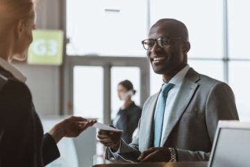 happy young businessman giving passport and ticket to staff at airport check in counter