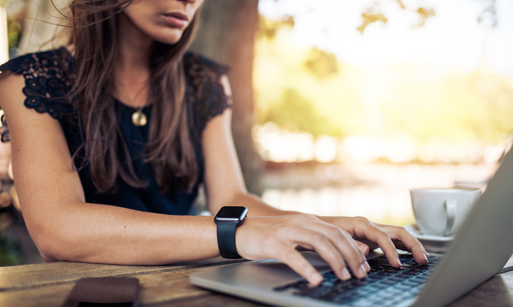 Young woman wearing smartwatch using laptop computer. Female working on laptop in an outdoor cafe.