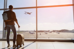 Thanksgiving Travel Myths: male tourist is standing in airport and looking at aircraft flight through window.