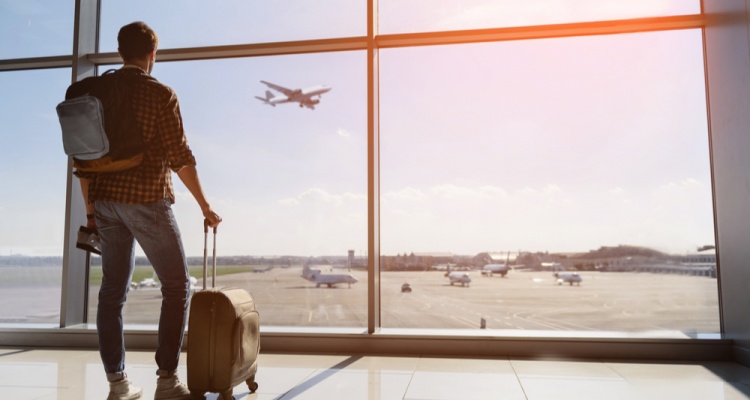 Thanksgiving Travel Myths: male tourist is standing in airport and looking at aircraft flight through window.