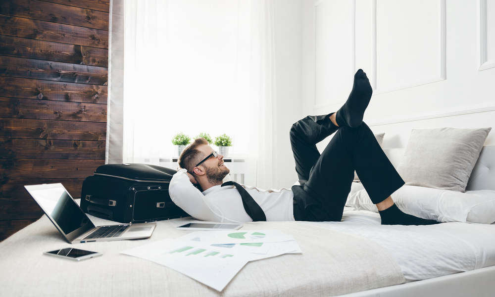 Young businessman on bed working with a laptop from his hotel room