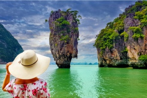 best pl;aces to travel solo in your 40s: Woman tourist with hat and floral dress looking at James Bond island in Thailand