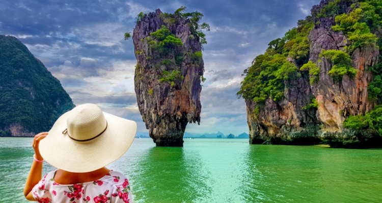 best pl;aces to travel solo in your 40s: Woman tourist with hat and floral dress looking at James Bond island in Thailand