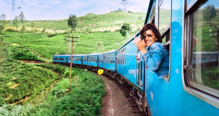 fun places to go visit in 2020: Happy smiling woman looks out from window traveling by train on most picturesque train road in Sri Lanka