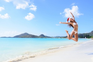 The Best Winter Getaways Where You Can Forget the Cold: girl jumping of joy and surprise on perfect white sand beach for winter holidays.