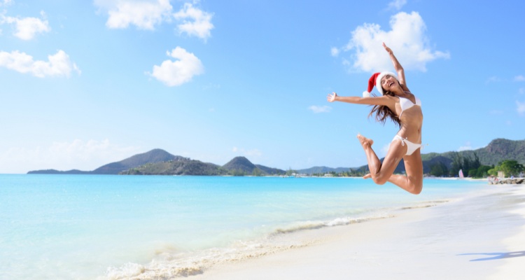 The Best Winter Getaways Where You Can Forget the Cold: girl jumping of joy and surprise on perfect white sand beach for winter holidays.