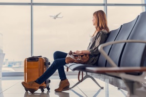 Everything You Need to Know About Open Jaw Flights: Beautiful young woman looking out window at flying airplane while waiting boarding on aircraft in airport lounge