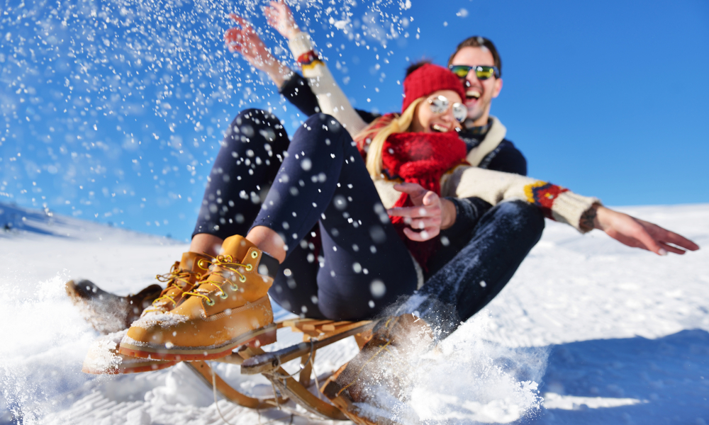 Young Couple Sledding And Enjoying On Sunny Winter Day