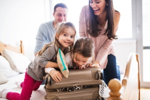 How to Save When You're Traveling with Kids: Young family with two children packing for holiday.