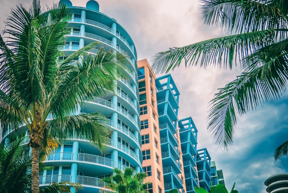 Architectural flat building Miami Style South Beach Florida image retro filtered Modern art deco condominium construction aqua and apricot color with palm trees against blue tropical sky background