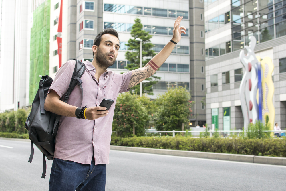 Young Man Holding Cellphone Hailing Uber Taxi