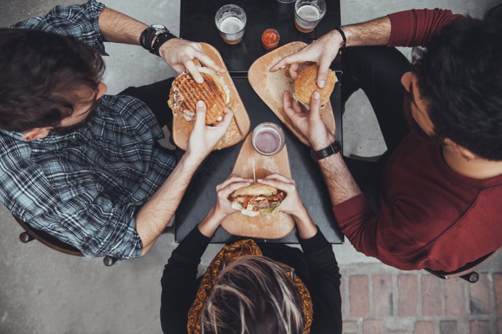 Hipster Friends In Fast Food Restaurant Eating Burgers. View From Above