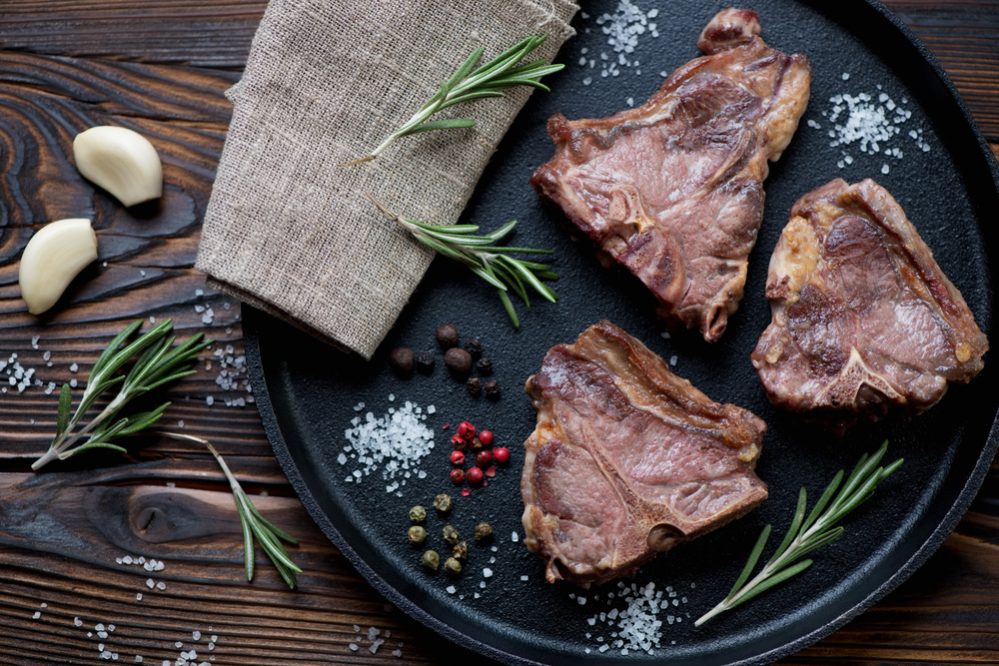 Top view of grilled T-bone lamb steaks in a frying pan, close-up