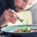 Chef in hotel or restaurant kitchen cooking, only hands. He is working on the micro herb decoration. Preparing tomato soup.