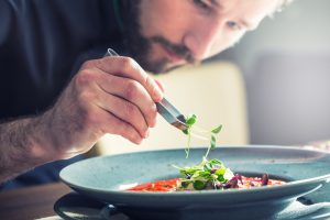 Chef in hotel or restaurant kitchen cooking, only hands. He is working on the micro herb decoration. Preparing tomato soup.