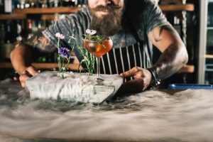 Happy barman is making cocktail with ice vapor at night club. Unique man. Bartender has a mustache and stylish hairstyle