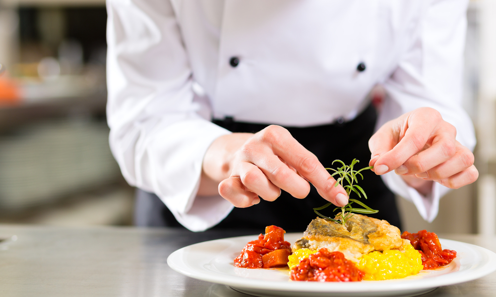 Female Chef in hotel or restaurant kitchen cooking, only hands, she is finishing a dish on plate