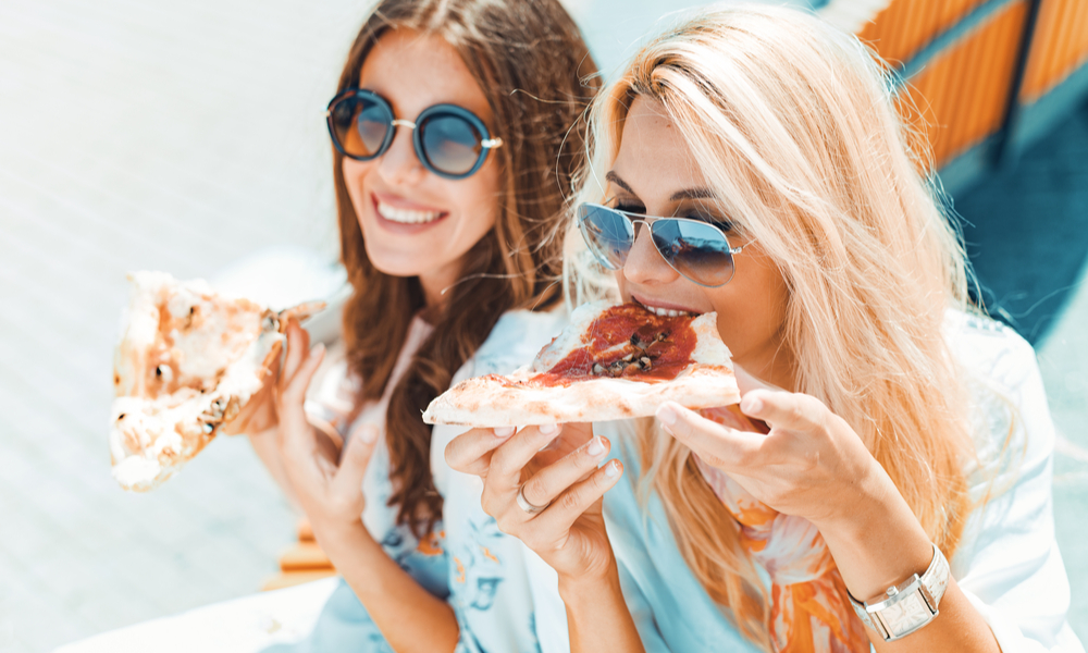 Portrait of two young women eating pizza outdoors,having fun together.