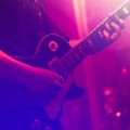 close up of singer playing electric guitar and singing on stage over happy fans crowd waving hands at concert in night club