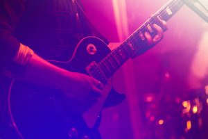 close up of singer playing electric guitar and singing on stage over happy fans crowd waving hands at concert in night club