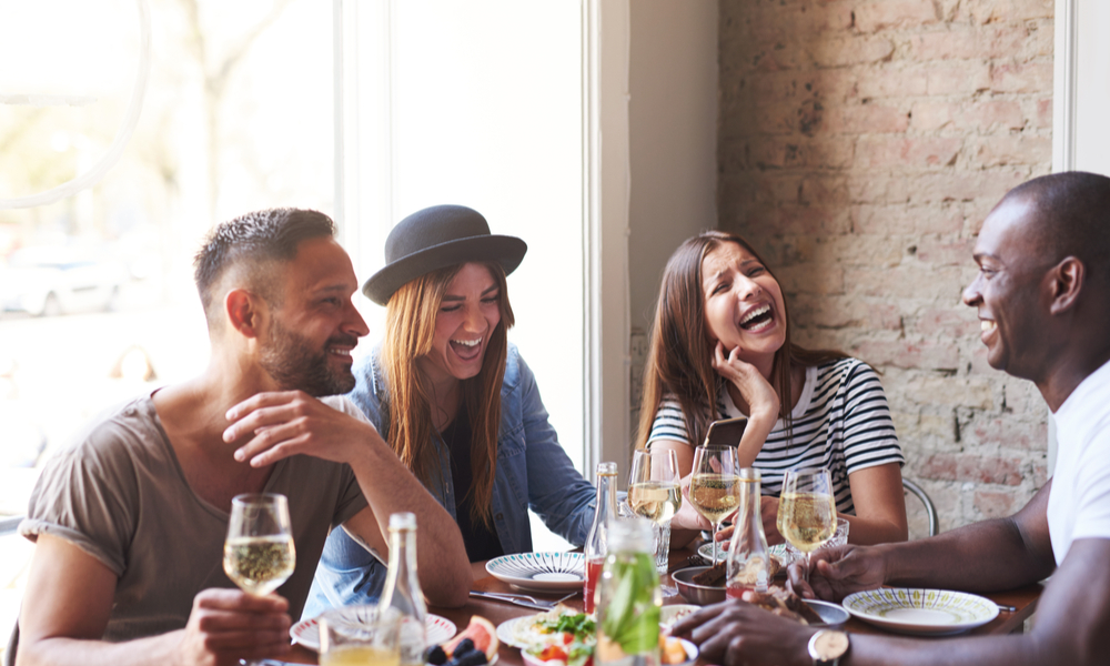 Group of young friends having fun and laughing while dining at table in restaurant.