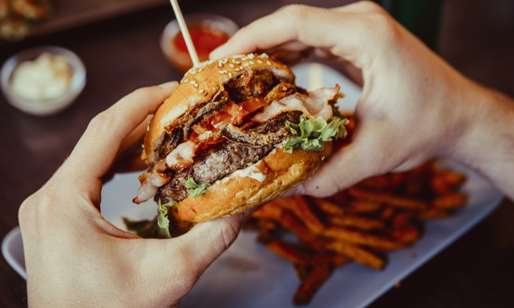 classic restaurants in denver: man holds burger with hands and sweet potato fries and dips on background